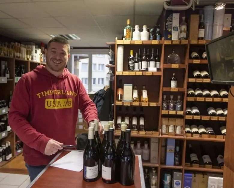 Caviste de l'équipe As du Vin à Dijon préparant des bouteilles de vin au comptoir pour un client.