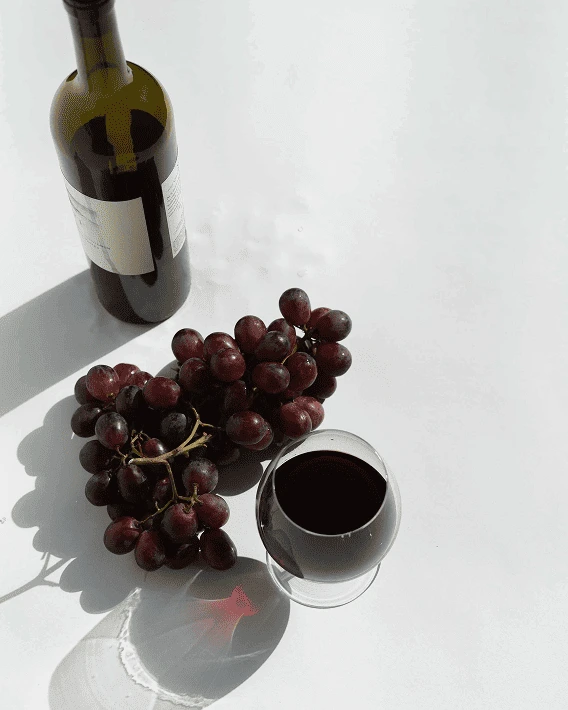 Une bouteille de vin rouge avec des raisins sur une surface blanche.